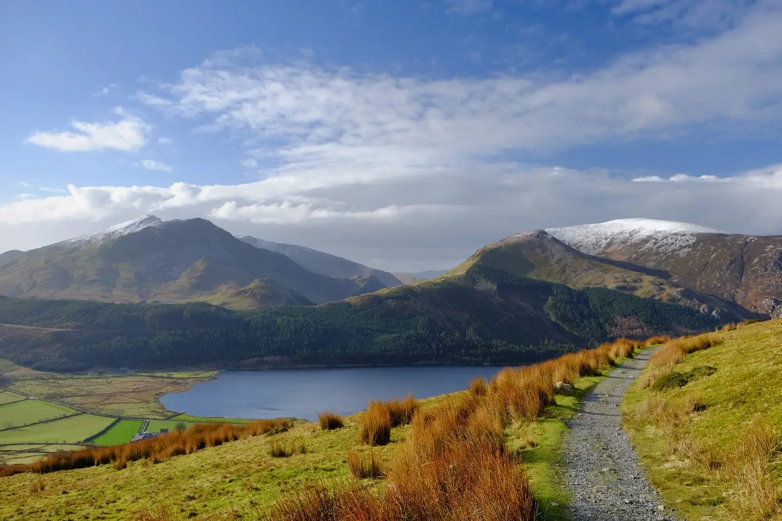 A path above a lake towards snow-dusted mountains in Snowdonia