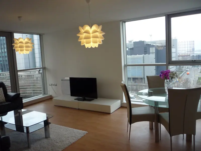 An open-plan living room with a sofa, a dining table and big windows