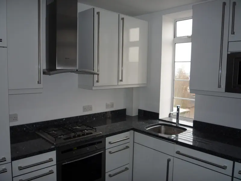 A white fitted kitchen with a gas hob and a window over the sink