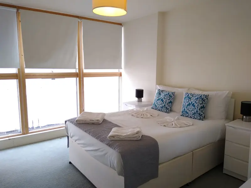 A bright double bedroom with tall windows, a made bed and bedside lamps